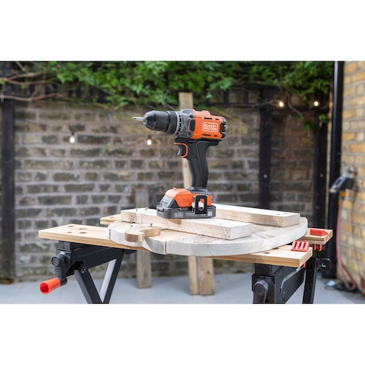 BLACK+DECKER cordless drill on a workbench outdoors, surrounded by wooden boards and tools.