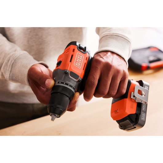 Person holding a BLACK+DECKER cordless drill in hand, preparing for use on a wooden surface.