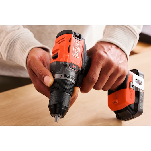 Person holding a BLACK+DECKER cordless drill on a wooden surface, with battery pack shown.