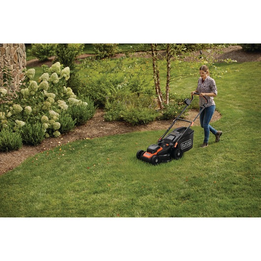 A person mowing the lawn with a BLACK+DECKER electric lawn mower in a green garden.