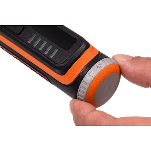 Close-up of a BLACK+DECKER photography device with an orange and black body, showing a person's fingers adjusting a gray and orange dial on the end.