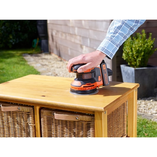 BLACKDECKER BDCROS18 cordless random orbital sander sanding wooden cabinet outdoors.