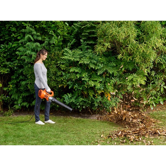 BLACKDECKER BEBL185 corded leaf blower in use outdoors, orange and black, clearing leaves from lawn.