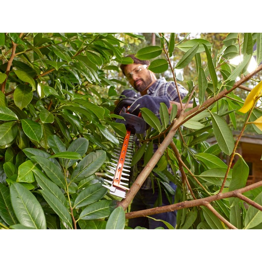BLACKDECKER BEHTS401 hedge trimmer cutting thick branches in dense green foliage, outdoor setting.