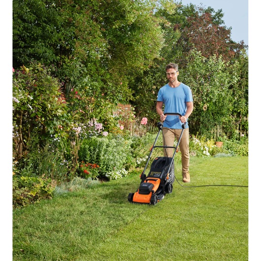 BLACKDECKER BEMWP340-QS lawn mower with orange and black design mowing grass in a garden outdoors.