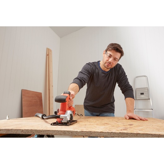 Photo of a person using a BLACKDECKER BES510 compact circular saw to cut wood on a workbench indoors.