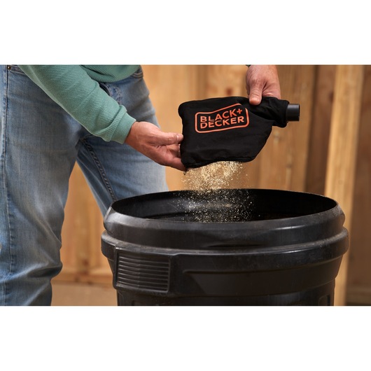 Photo of person emptying dust from BLACK+DECKER BES702 dust bag into a black trash bin.