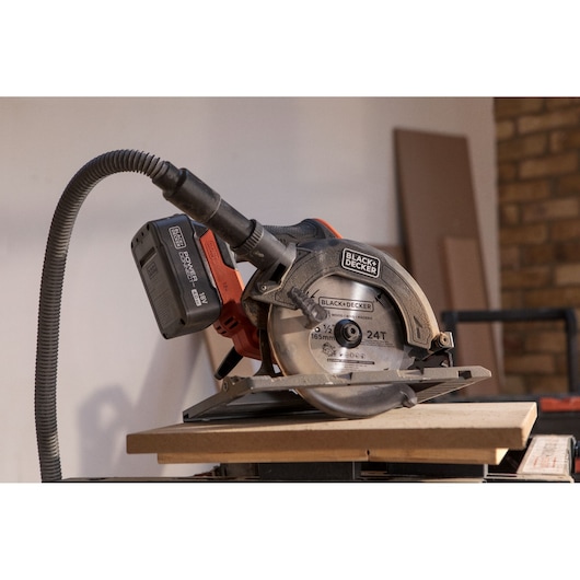 BLACK+DECKER cordless circular saw BLCCS78M1 with dust extraction hose cutting wood in workshop setting.