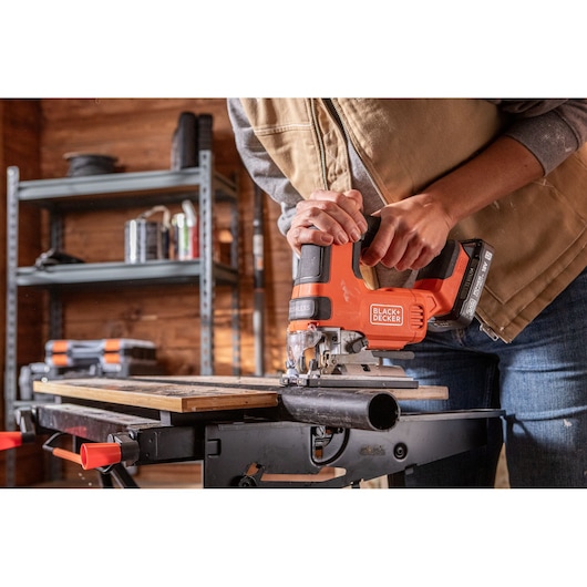 Photo of BLACKDECKER BLCJS78E1 cordless jigsaw cutting wood on a workbench in a workshop setting.