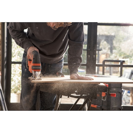 BLACKDECKER BLCJS78E1 jigsaw cutting wood on workbench, close-up action, dust particles, indoor workshop.