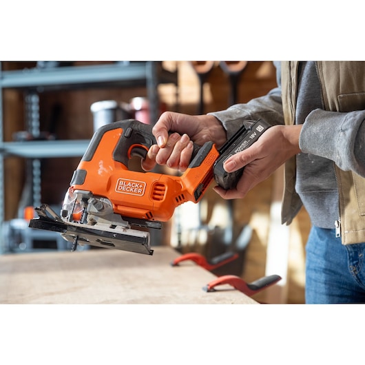 Photo of BLACK+DECKER BLCJS78E1 cordless jigsaw held in hand, battery being installed, workshop background.