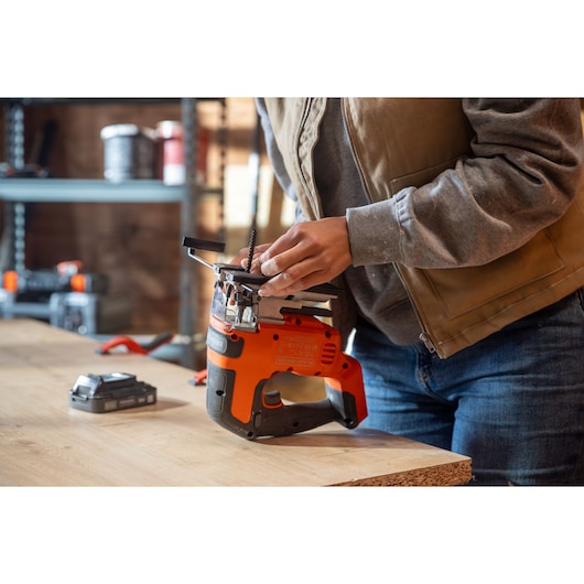 Photo of a person adjusting a BLACK+DECKER BLCJS78E1 jigsaw on a wooden workbench in a workshop.
