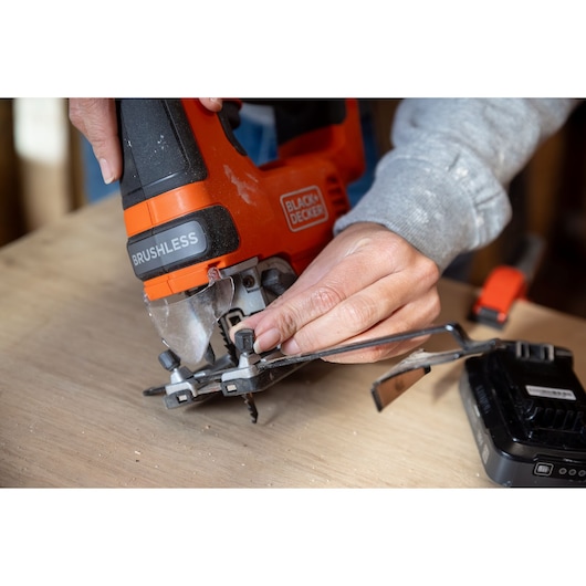 Close-up of BLACKDECKER BLCJS78E1 jigsaw being adjusted by hand on wood surface.