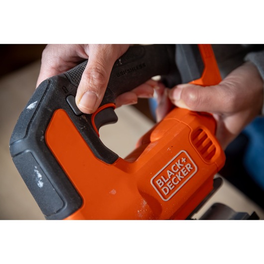 Close-up photo of BLACK+DECKER BLCJS78E1 jigsaw handle in use, showing orange and black grip and trigger.