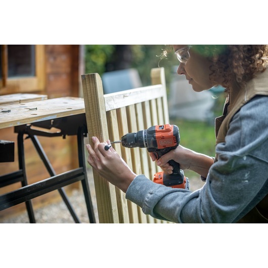 Person using BLACK+DECKER BLD782E1K cordless drill on wooden fence outdoors.