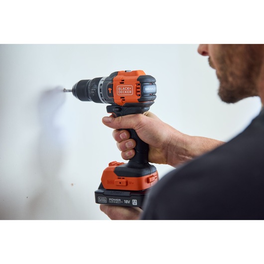 Photo of a BLACK+DECKER BLD783N cordless drill in use against a white wall, orange and black design, side angle.