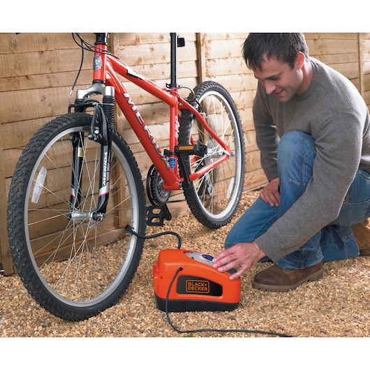 A man inflates a bicycle tyre using the BLACK+DECKER 160 PSI AC/DC Multi Purpose Air Station