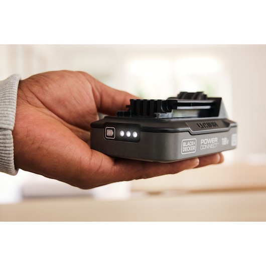 A hand holding the BLACK+DECKER® POWERCONNECT™ 18V 2.0 Ah State of Charge Li-ion Battery, showing the illuminated state of charge display.