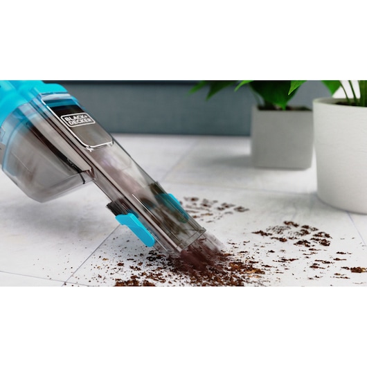 Close-up of the BLACK+DECKER Dustbuster vacuuming soil from a tile floor.