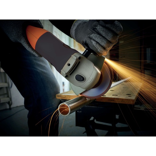 A person wearing gloves is using a BLACK+DECKER angle grinder to cut a metal pipe, with sparks flying from the cutting area.