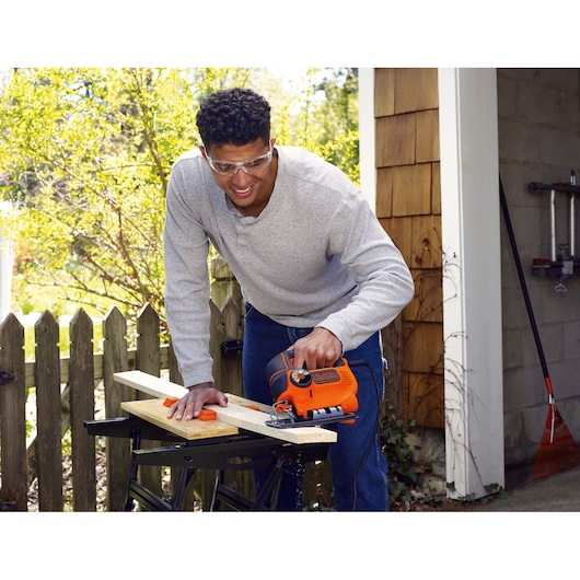 A man cuts a wooden plank using the BLACK+DECKER® 550W AUTOSELECT® Pendulum Jigsaw.