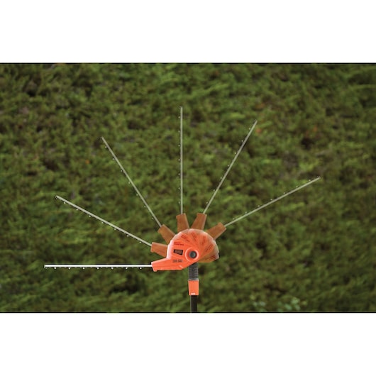 An orange BLACK+DECKER hedge trimmer with adjustable blade positions shown outdoors against a green hedge background.